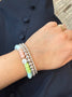 Load image into Gallery viewer, Model wearing Anzie pastel opal bead bracelet with rondelle-cut opal gemstones, rhodium-plated sterling silver charm, white enamel detailing, and clear topaz stones stacked with silver beaded bracelets. 

