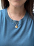Load image into Gallery viewer, Model wearing the Anne Sportun organic coin charm in 18K yellow gold on a gold chain, featuring an off-center star set with a single pink sapphire.
